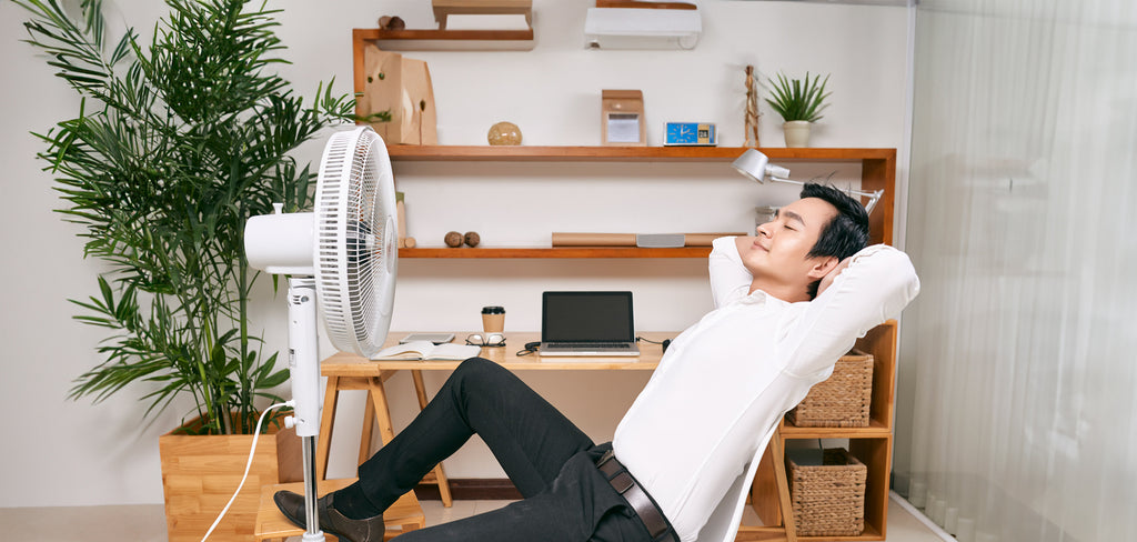 businessman relaxing on a chair infront of a stand fan blowing on him