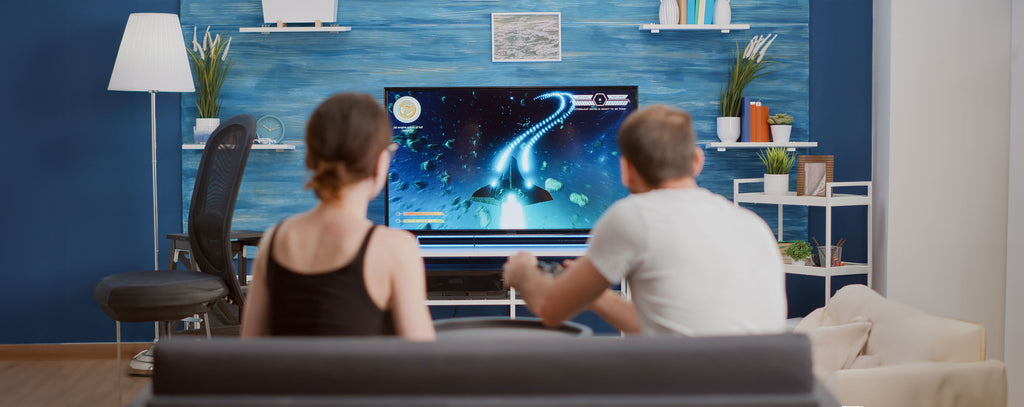 Girlfriend eating popcorn and supporting boyfriend gamer playing console video game first person shooter on tv while sitting on sofa. Couple on couch enjoying gaming simulation in modern living room.