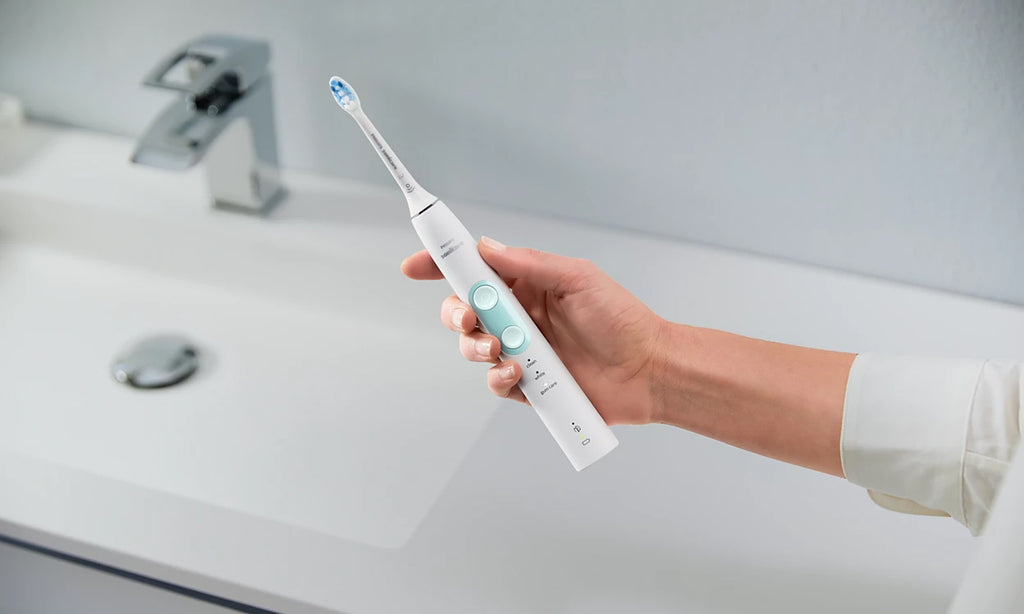 holding a white electric toothbrush in a bathroom